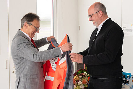 Der Präsident des DRK Calw überreicht Thomas Seeger eine Jacke des DRK.