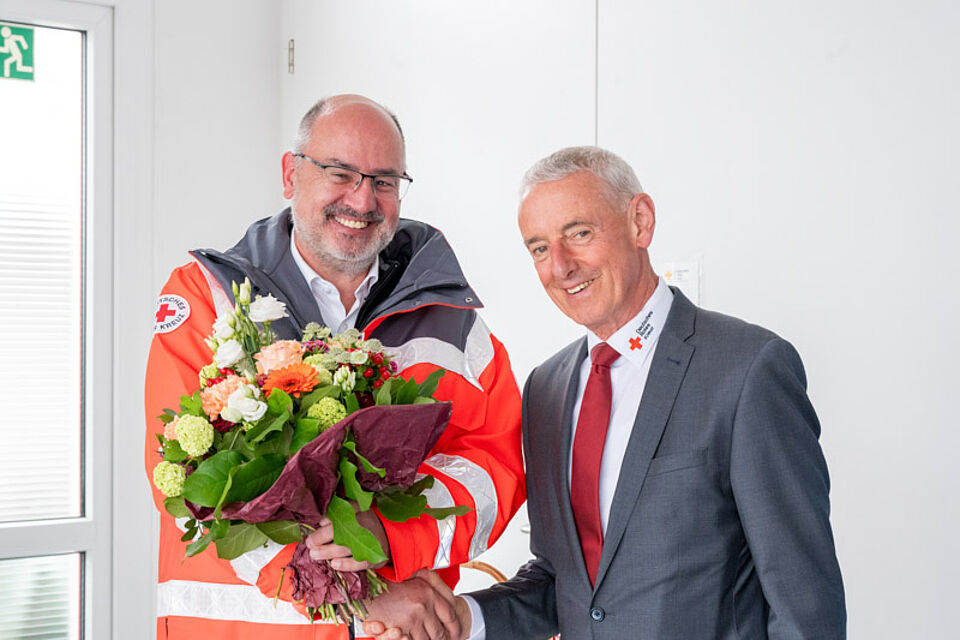 Verabschiedung Seeger Zwei Männer aus dem DRK Calw reichen sich die Hand, einer hält einen Blumenstrauß.