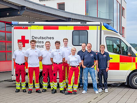 Sechs junge Menschen in Rettungsdienstkleidung mit ihren Ausbildern vor einem Rettungswagen.