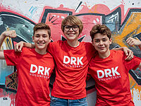 drei fröhliche Jugendliche in roten T-Shirts vor einer bunten Wand